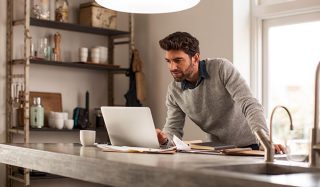 明るくて快適なホームオフィスで、LEDタスク照明を使って効率的にリモートワークをこなす男性の様子です。